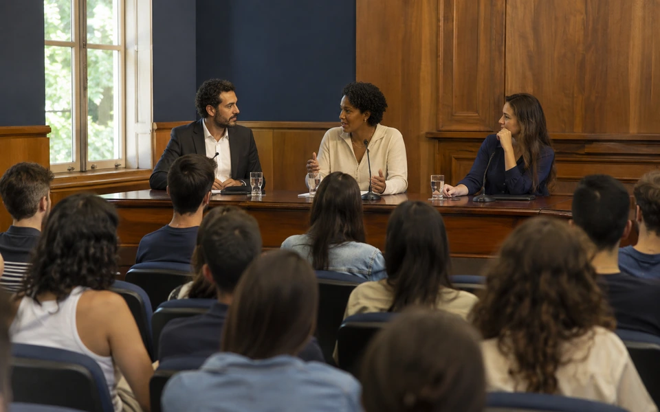 Cena ilustrativa de um painel acadêmico com participantes e plateia